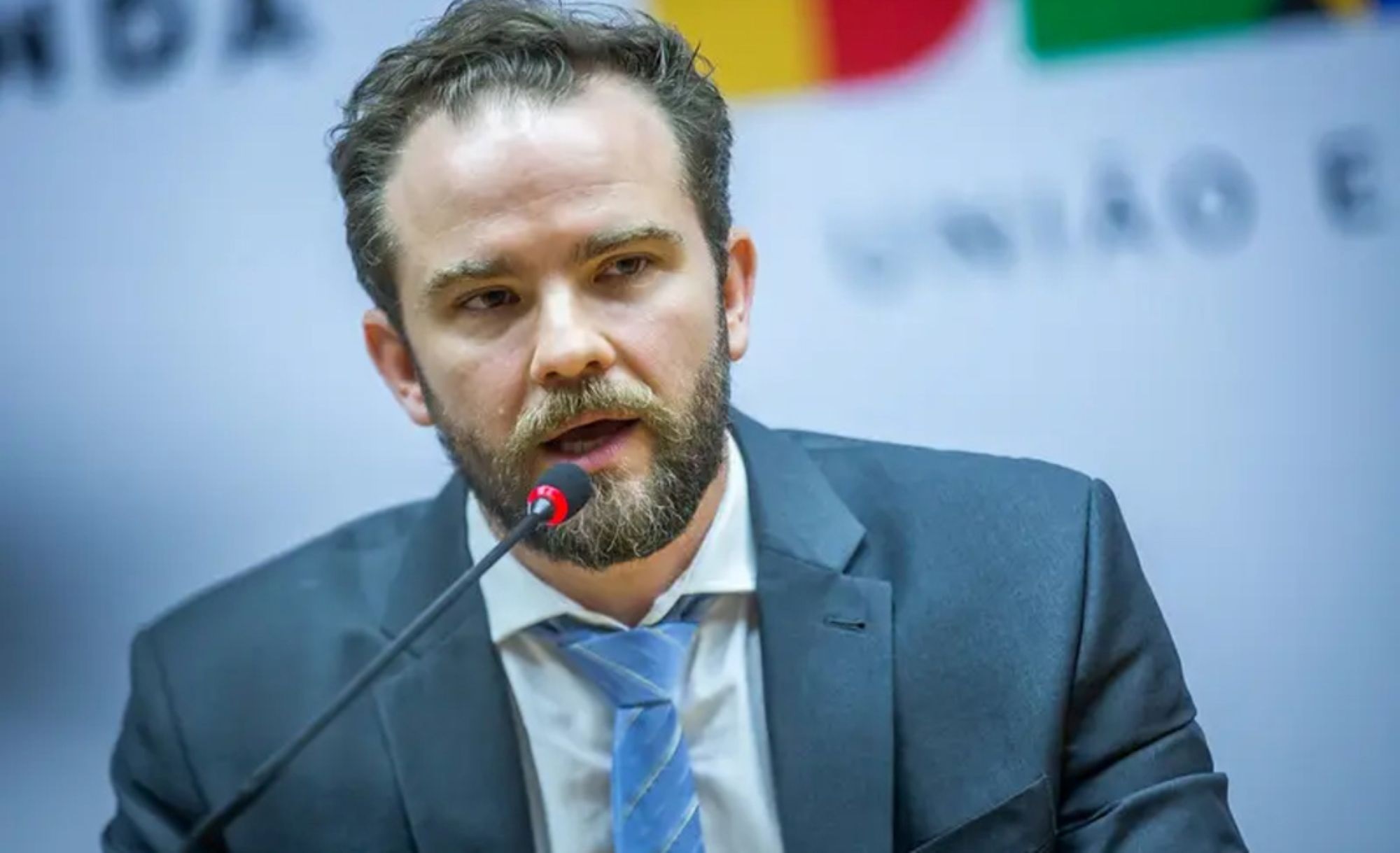 ministro da Fazenda, Dario Durigan, falando em microfone, sério, sem olhar para a câmera