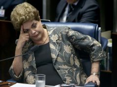 Dilma Rousseff sentada, com o rosto apoiado sobre uma das mãos, séria
