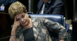 Dilma Rousseff sentada, com o rosto apoiado sobre uma das mãos, séria