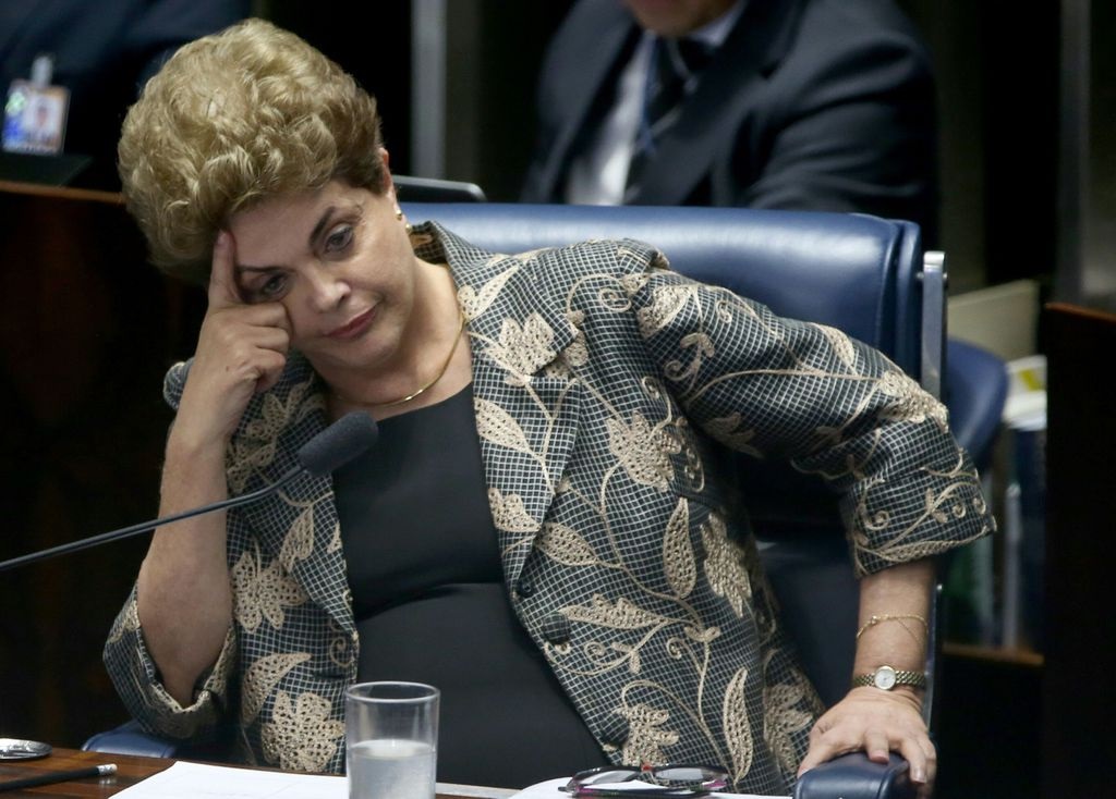 Dilma Rousseff sentada, com o rosto apoiado sobre uma das mãos, séria