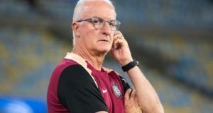 técnico Dorival Júnior sério, de óculos de grau, com uma mão em uma orelha