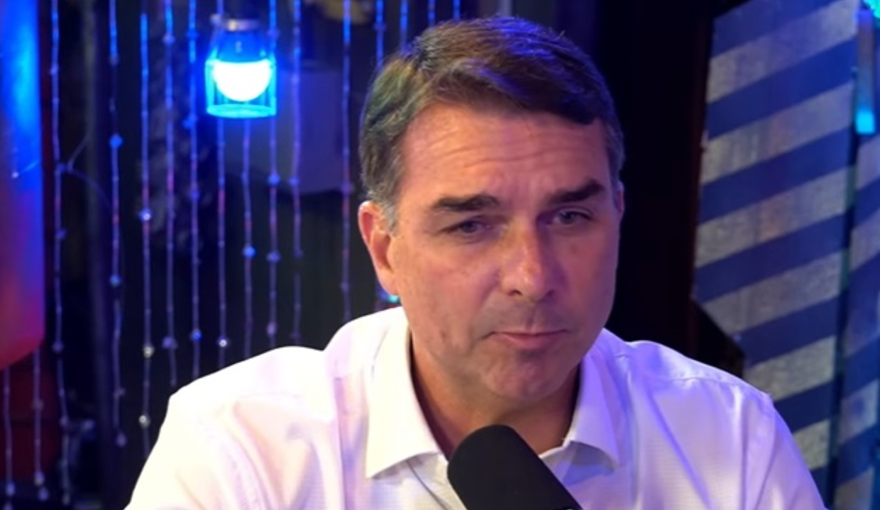 O pré-candidato à Presidência da República Flávio Bolsonaro (PL) falando em microfone, sério, de roupa clara