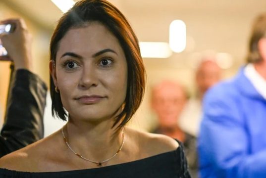 A ex-primeira-dama Michelle Bolsonaro no canto esquerdo da foto, com expressão de espanto