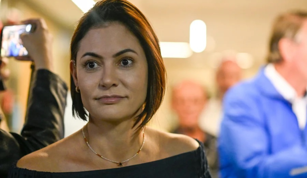 A ex-primeira-dama Michelle Bolsonaro no canto esquerdo da foto, com expressão de espanto