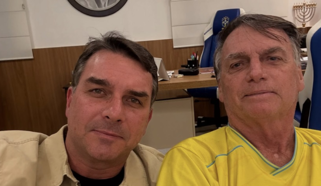 Flávio Bolsonaro e Jair Bolsonaro posando para selfie, lado a lado, ambos sem sorrir
