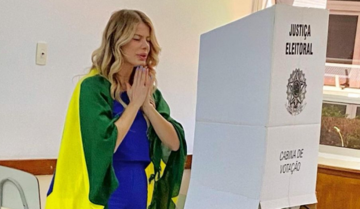 A ex-atriz Karina Bacchi com bandeira do Brasil, em posição de oração