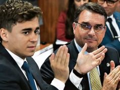 O deputado federal Nikolas Ferreira (PL-MG) e o senador Flávio Bolsonaro (PL-RJ) sentados lado a lado, o primeiro batendo palmas