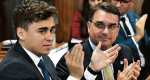 O deputado federal Nikolas Ferreira (PL-MG) e o senador Flávio Bolsonaro (PL-RJ) sentados lado a lado, o primeiro batendo palmas