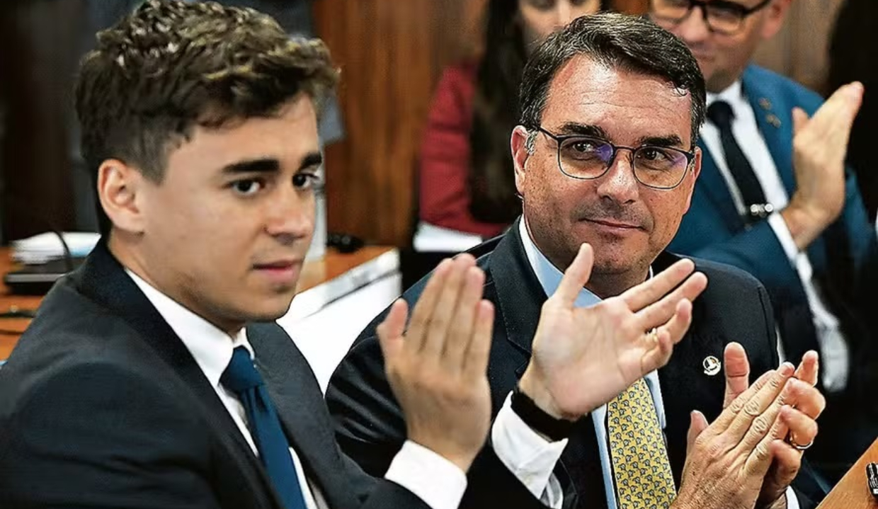 O deputado federal Nikolas Ferreira (PL-MG) e o senador Flávio Bolsonaro (PL-RJ) sentados lado a lado, o primeiro batendo palmas