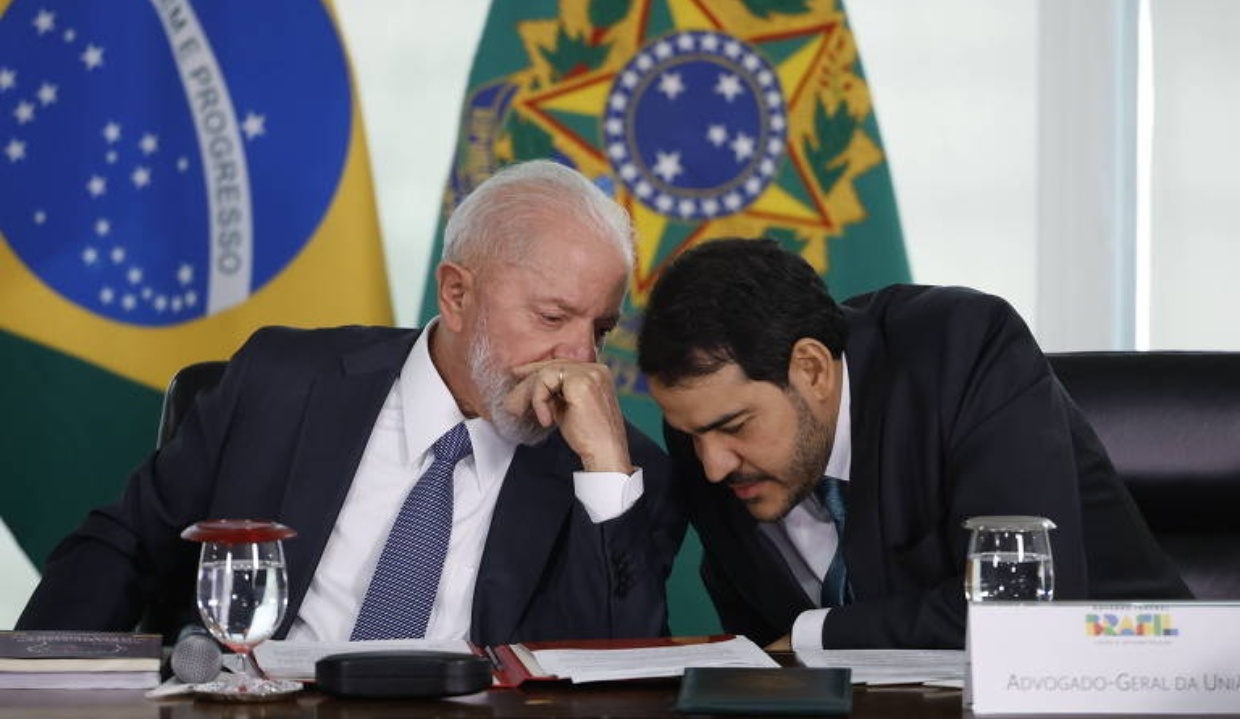 O presidente Luiz Inácio Lula da Silva (PT) e Jorge Messias, da AGU, conversando ao pé do ouvido, sentados lado a lado