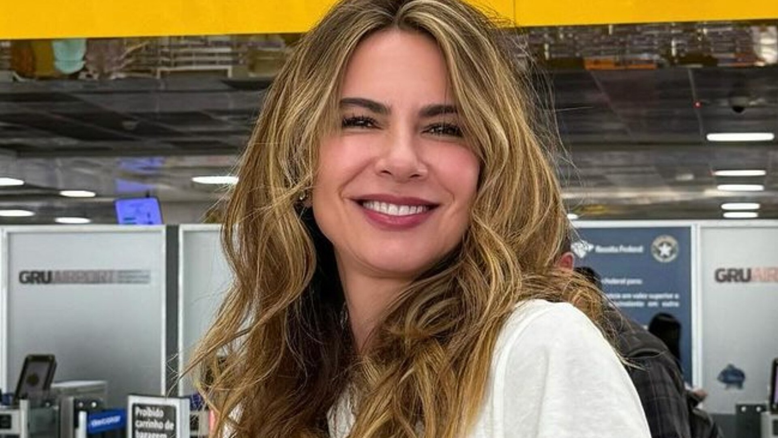 Luciana Gimenez de branco, de cabelo solto, sorrindo para a câmera