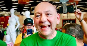 Luciano Hang de braços cruzados, rindo, sem olhar para a câmera, de camiseta verde