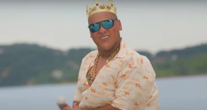 MC Ryan dançando, de óculos escuros e coroa, de camisa estampada