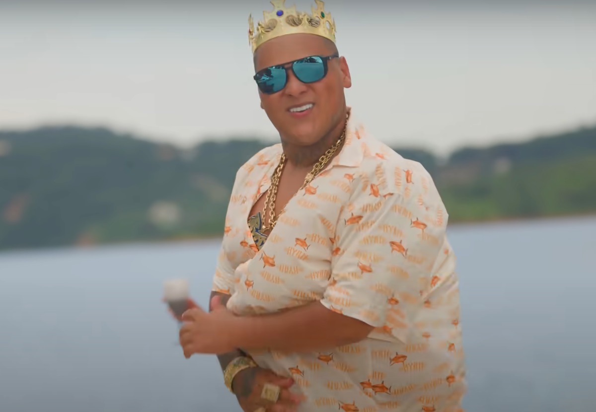 MC Ryan dançando, de óculos escuros e coroa, de camisa estampada