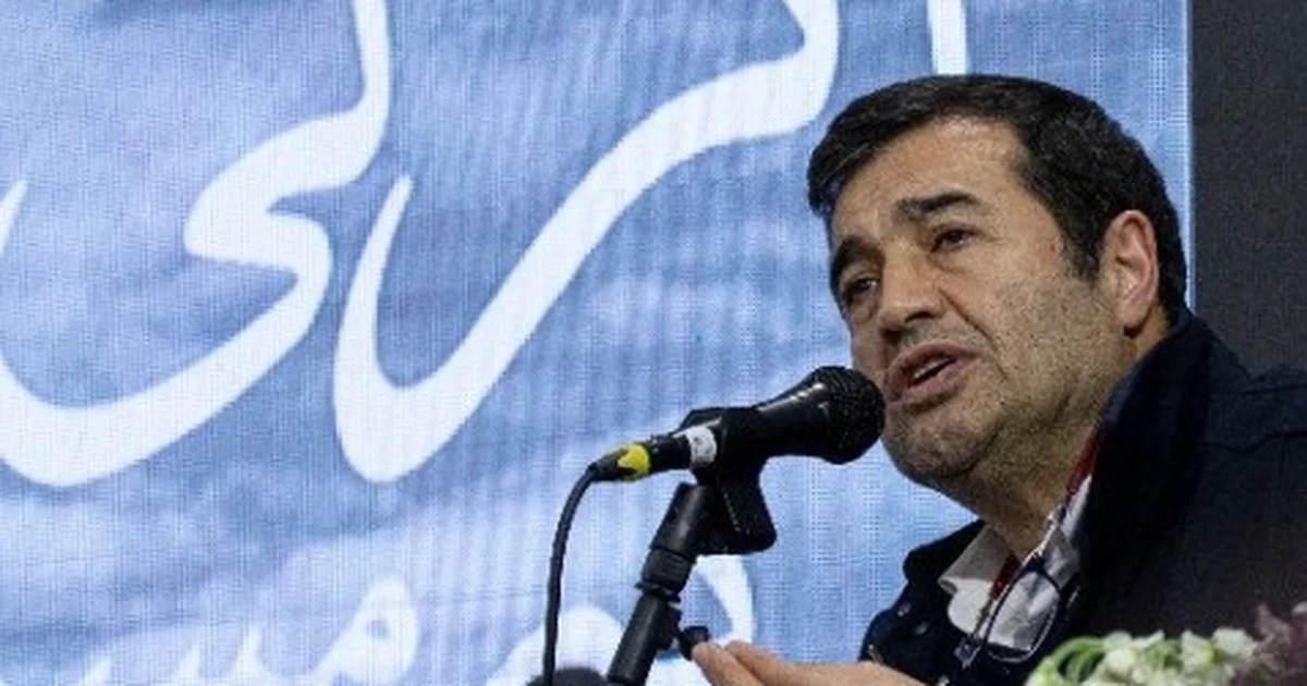 Ahmad Donyamali, ministro do Esporte e da Juventude do Irã, falando em microfone, sério, no canto direito de foto