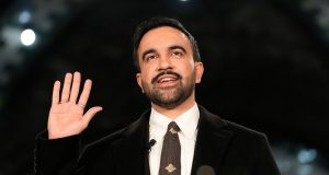 O prefeito de Nova York, Zohran Mamdani, sorrindo e acenando, de roupa social preta e branca