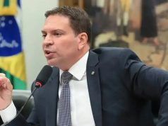 Alexandre Ramagem de perfil, sentado, falando e gesticulando, sério