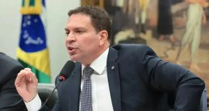 Alexandre Ramagem de perfil, sentado, falando e gesticulando, sério