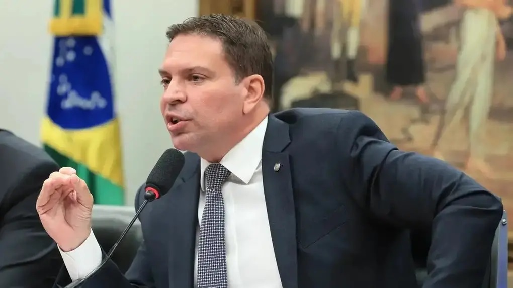 Alexandre Ramagem de perfil, sentado, falando e gesticulando, sério