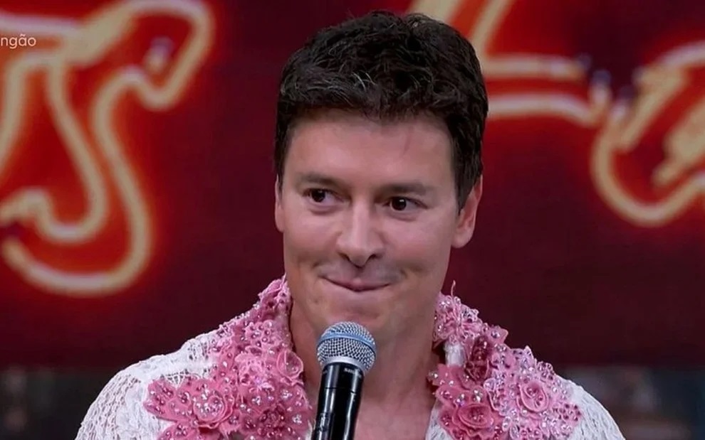 Rodrigo Faro sorrindo, segurando microfone, sem olhar para a câmera