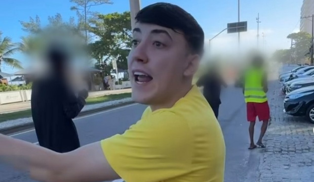 influencer Luan Lennon de perfil, falando e apontando, na rua, de camiseta amarela
