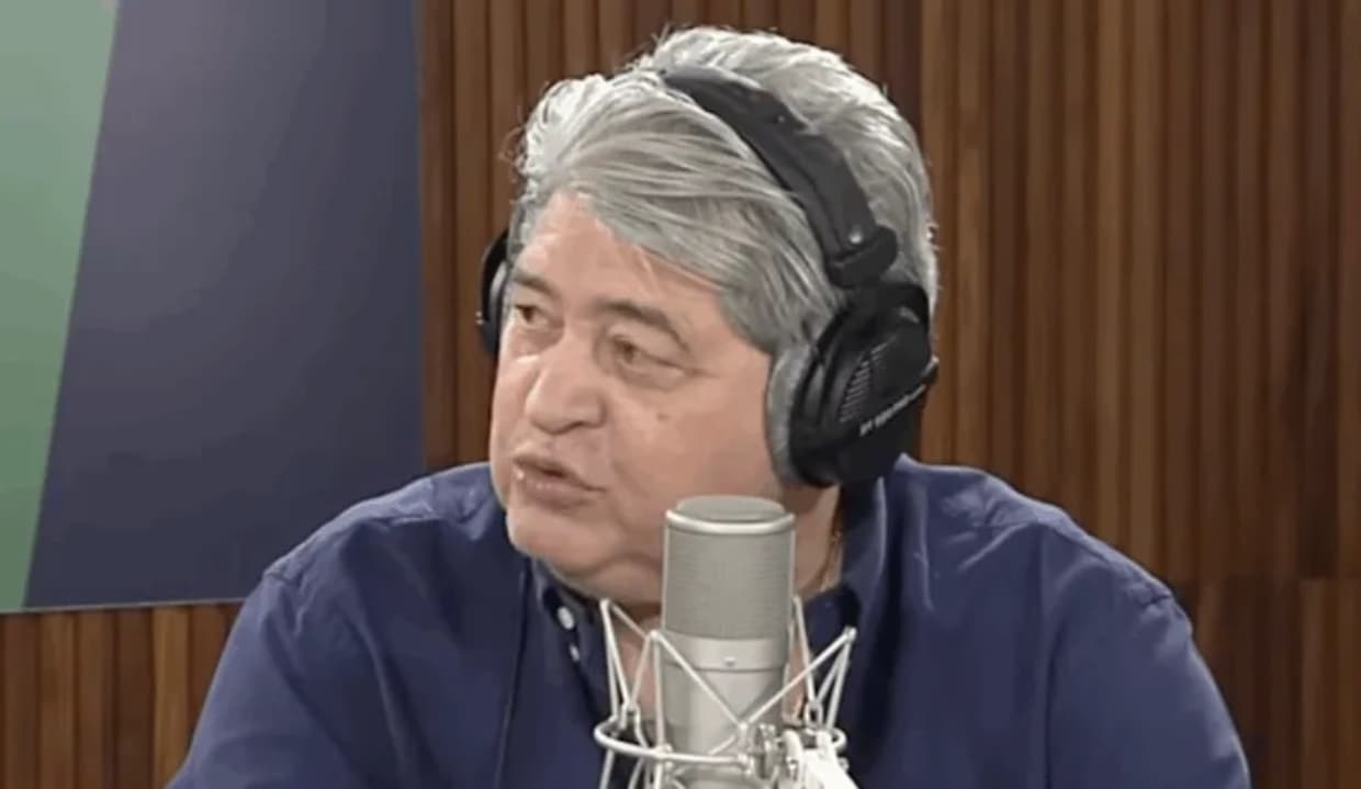 José Luiz Datena de fone, olhando para o lado e falando em microfone, sério