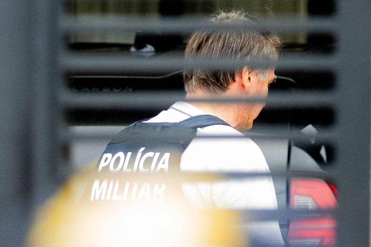 Homem de colete preto da Polícia Militar próximo a veículo escuro
