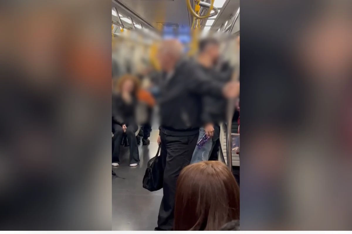 Homem em pé em vagão de metrô com passageiros ao redor e rostos borrados