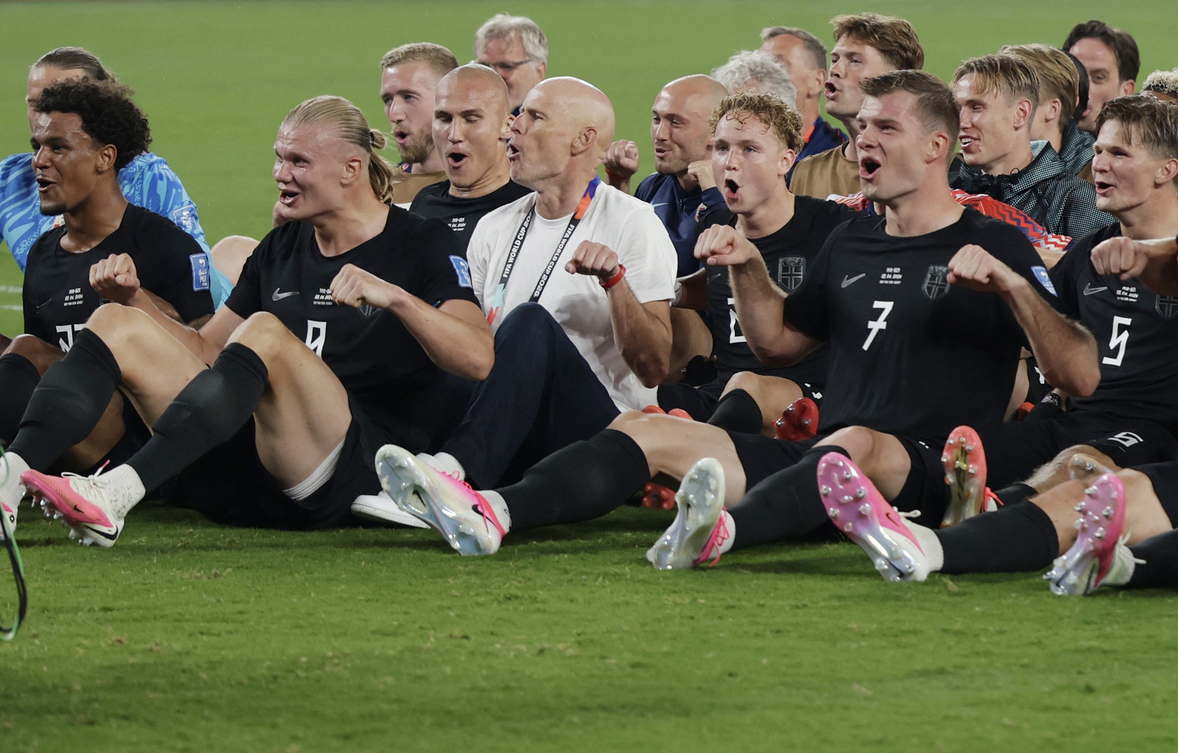 Jogadores da Noruega sentados no gramado durante coreografia com a torcida