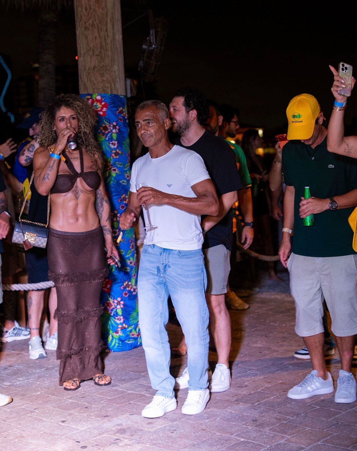 Romário em festa em Miami segurando uma taça ao lado de uma mulher