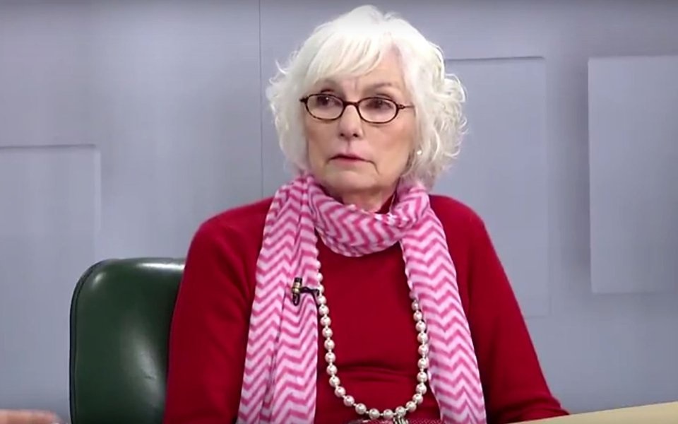 Bia Pardi de roupa vermelha e rosa, de óculos, olhando para o lado