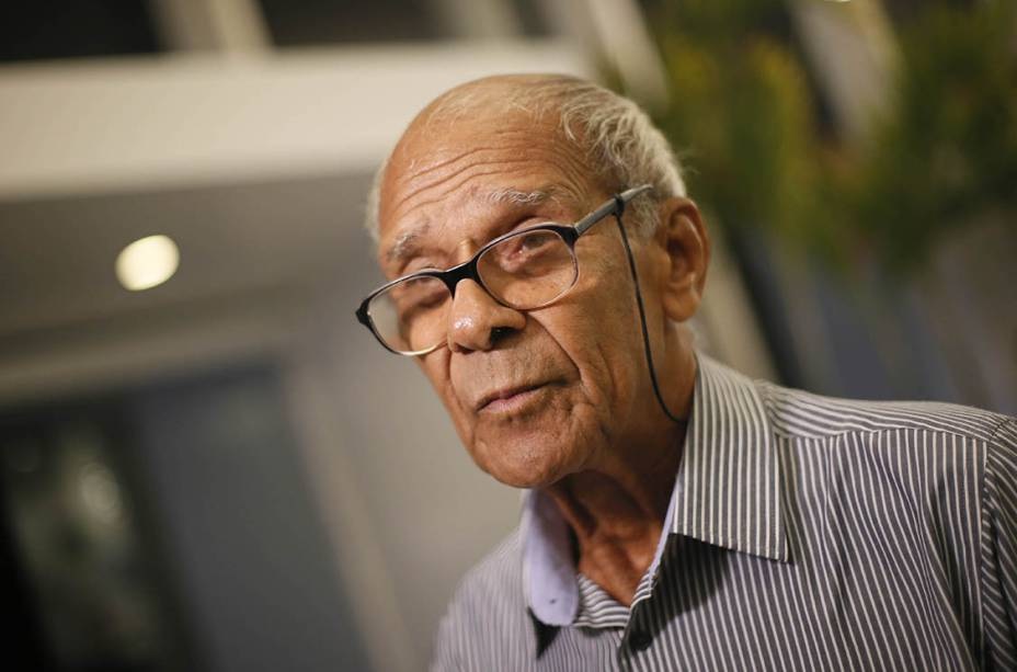 O ex-zagueiro Brito de óculos de grau e camisa social listrada, sério, sem olhar para a câmera