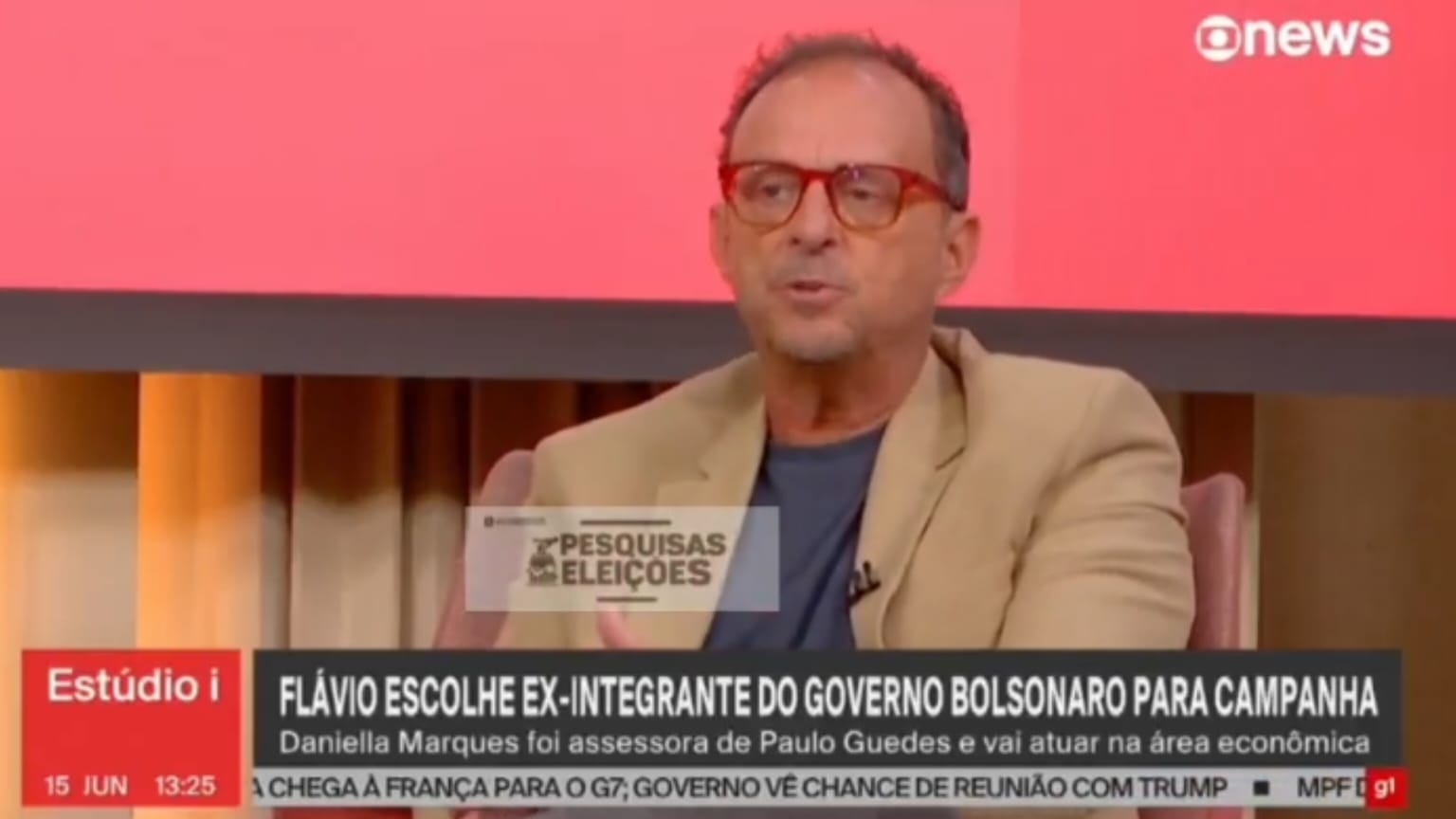 Octavio Guedes falando, sério, de óculos de grau e roupa social bege