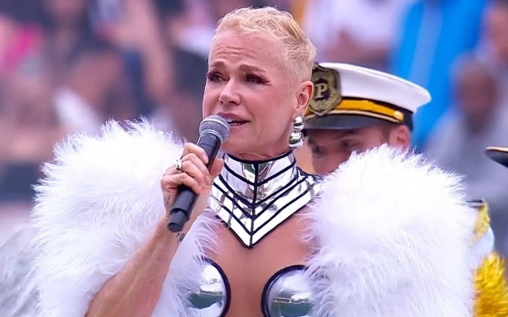 Xuxa Meneghel falando em microfone e olhando para o lado