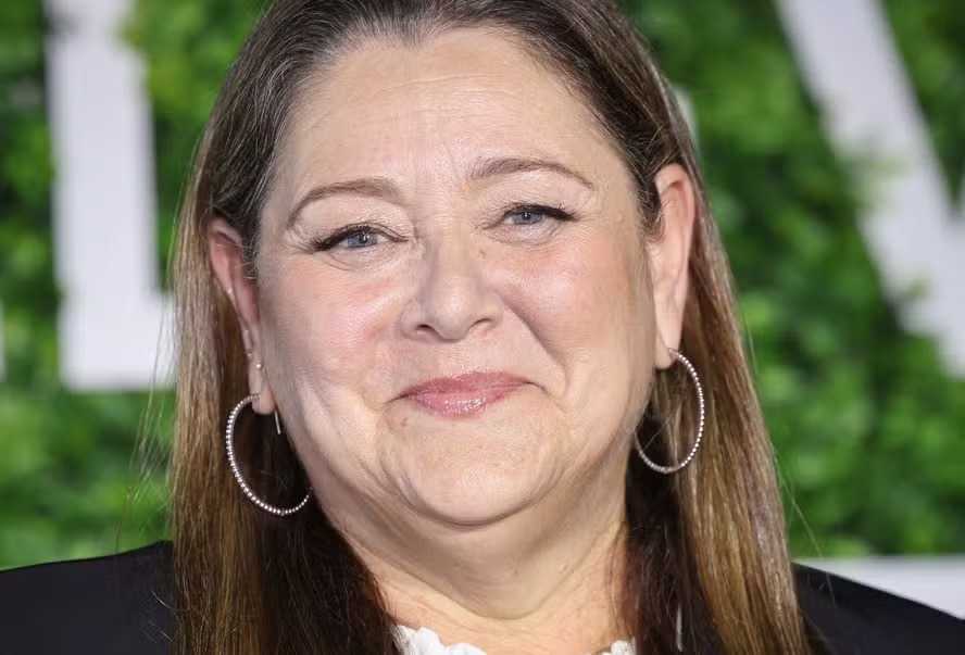 Camryn Manheim com cabelos presos, blusa escura e óculos