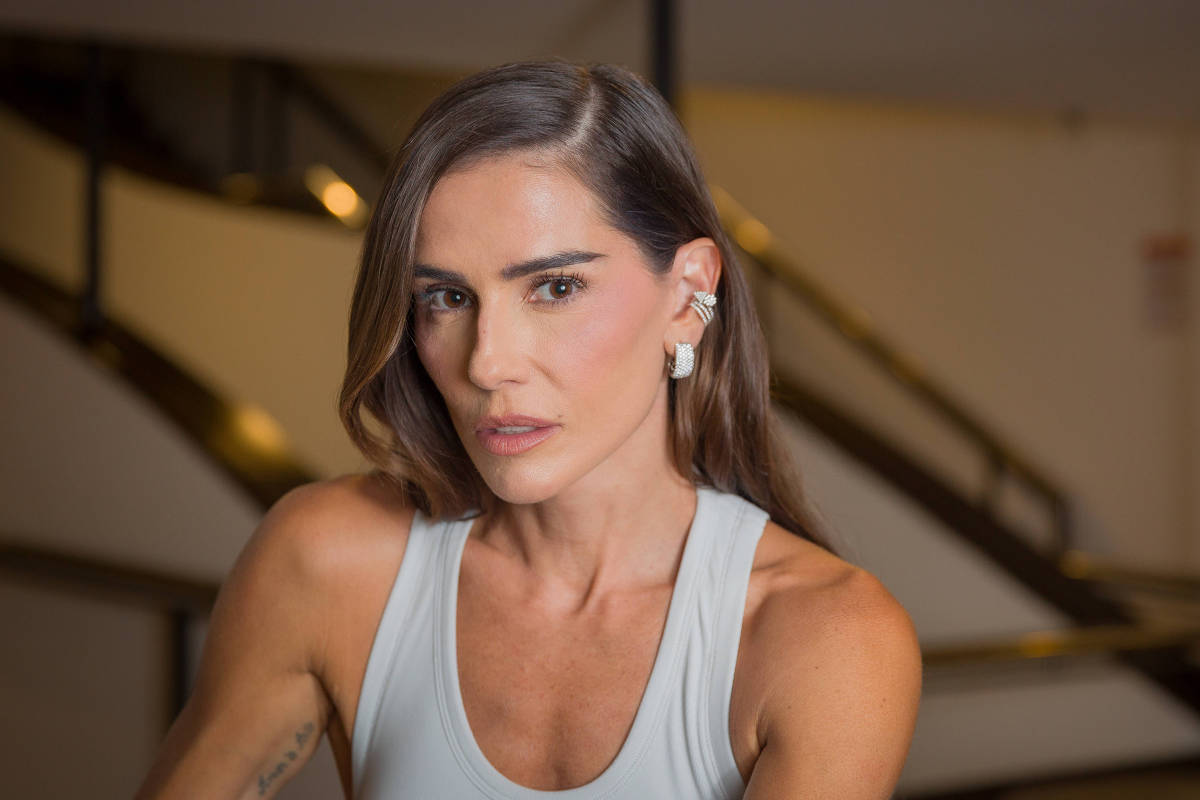 Deborah Secco em ambiente interno, com blusa clara e fone de ouvido