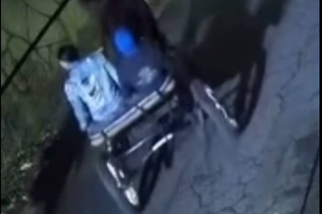 Duas pessoas caminham em uma rua durante a noite; uma delas empurra uma cadeira de rodas vazia