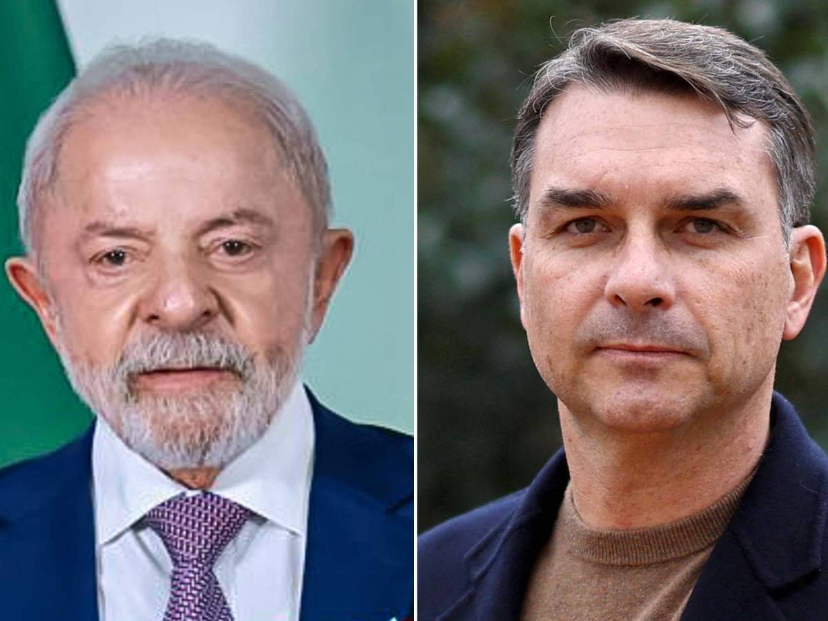 Lula de terno azul e gravata roxa ao lado de Flávio Bolsonaro com suéter marrom e casaco preto