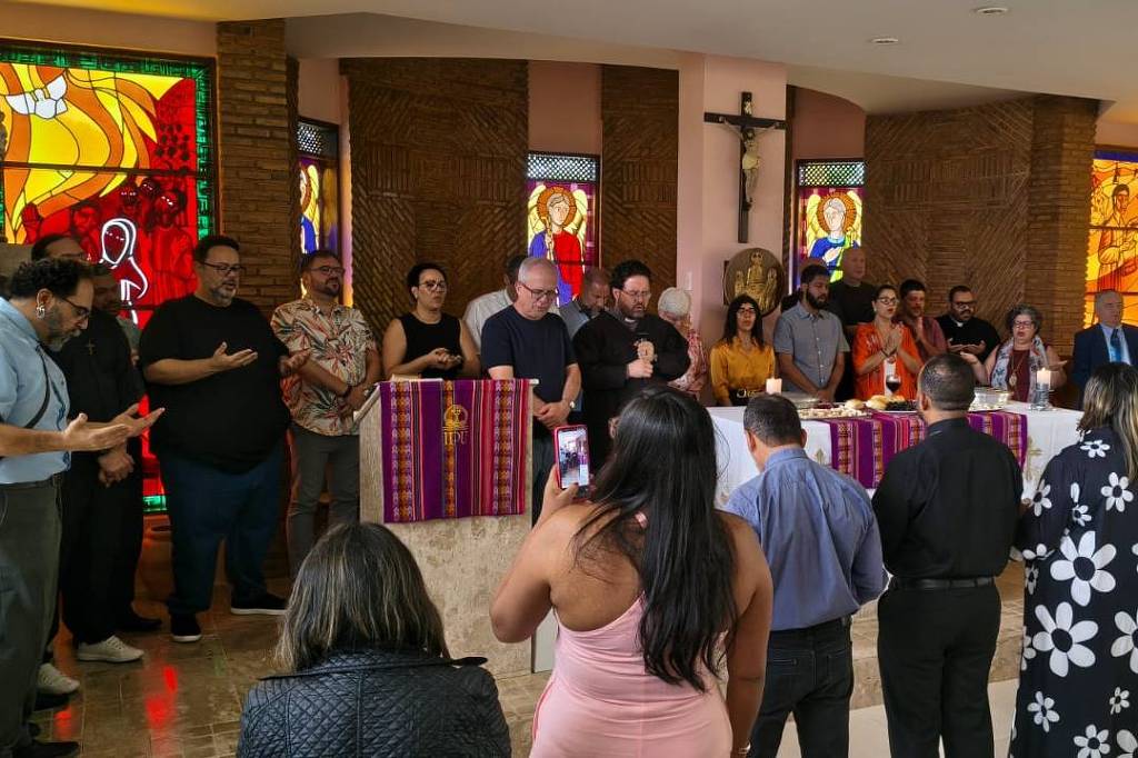 Pessoas reunidas em círculo dentro de igreja com vitrais coloridos e crucifixo