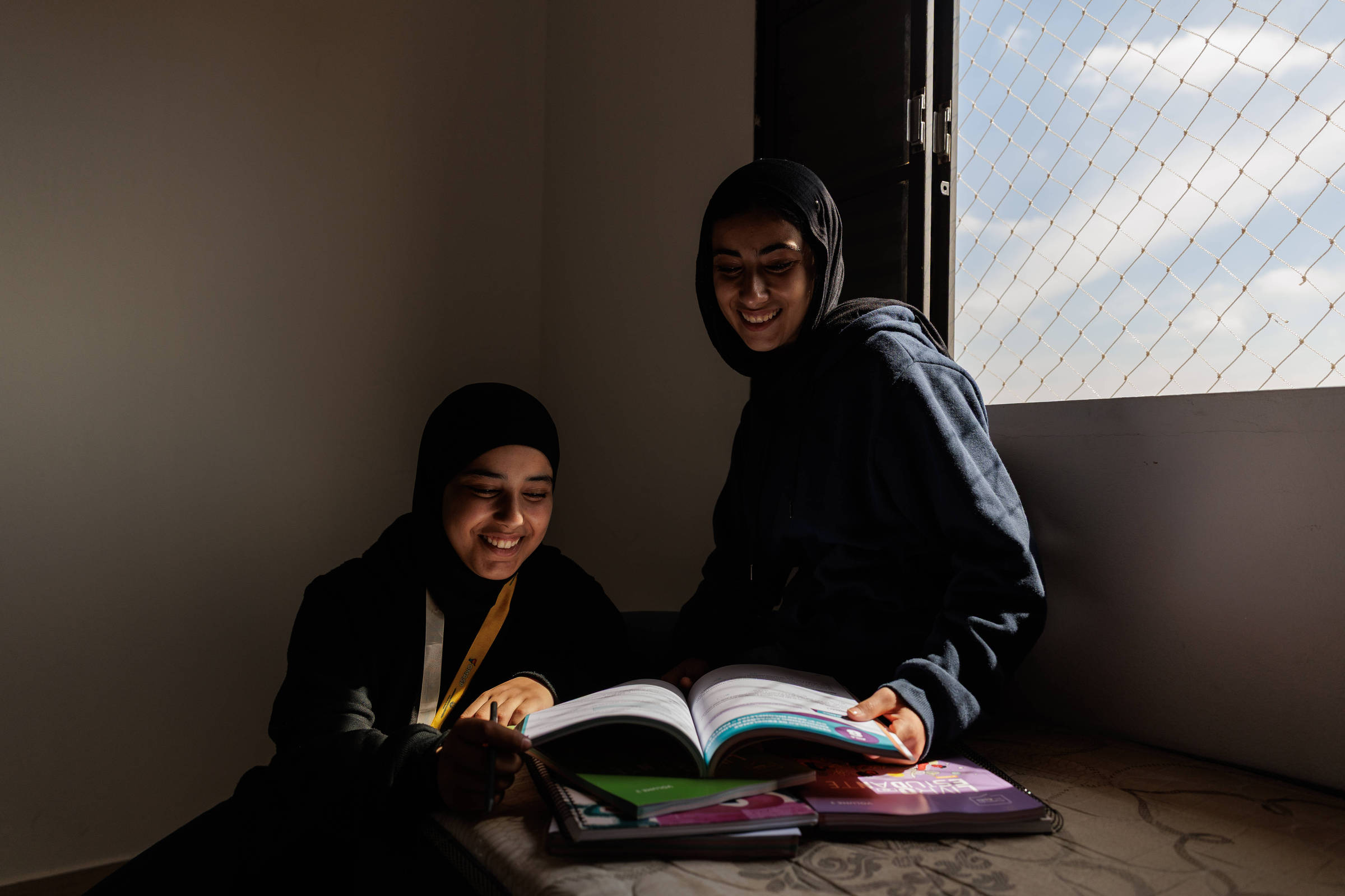 Tala e Dana Awad usam hijab e leem livros sentadas perto de uma janela