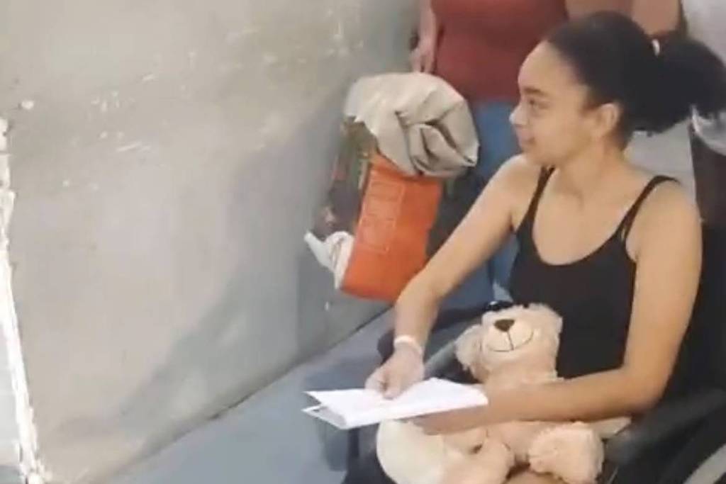 Marcela Vitória sentada em cadeira de rodas segurando ursinho de pelúcia e papéis