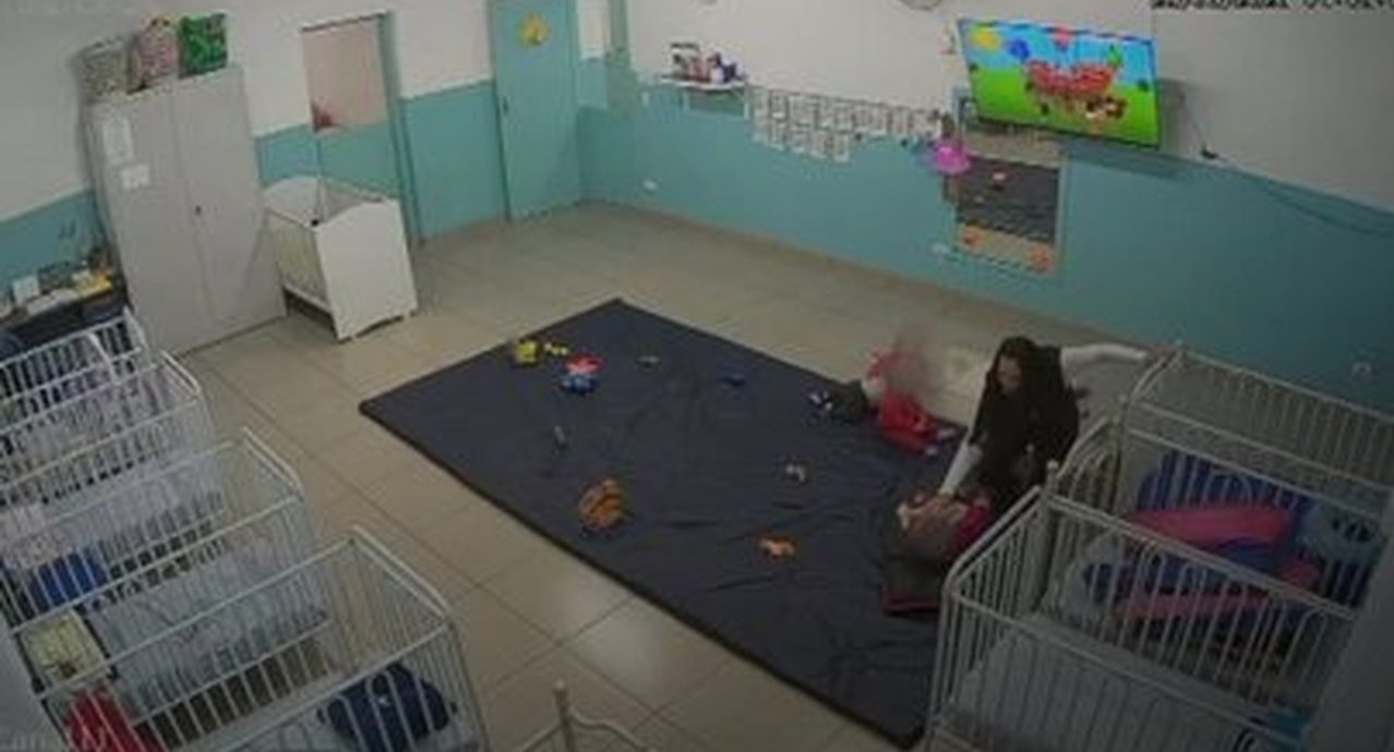 Sala de creche com criança e funcionária captadas por câmera de monitoramento