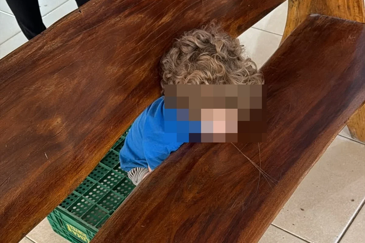 Criança com a cabeça presa no vão de um banco de madeira