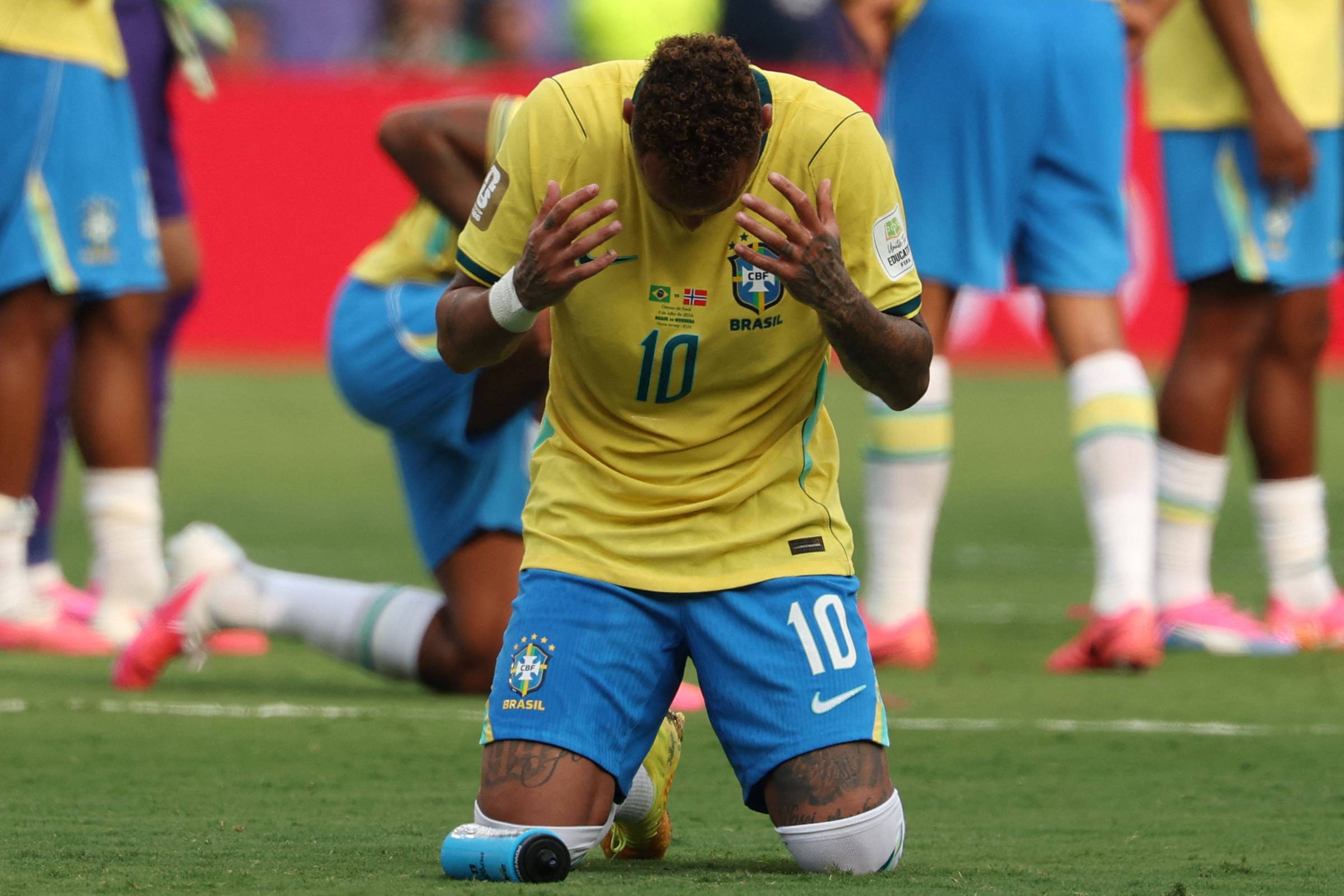 Neymar ajoelhado no gramado com as mãos juntas