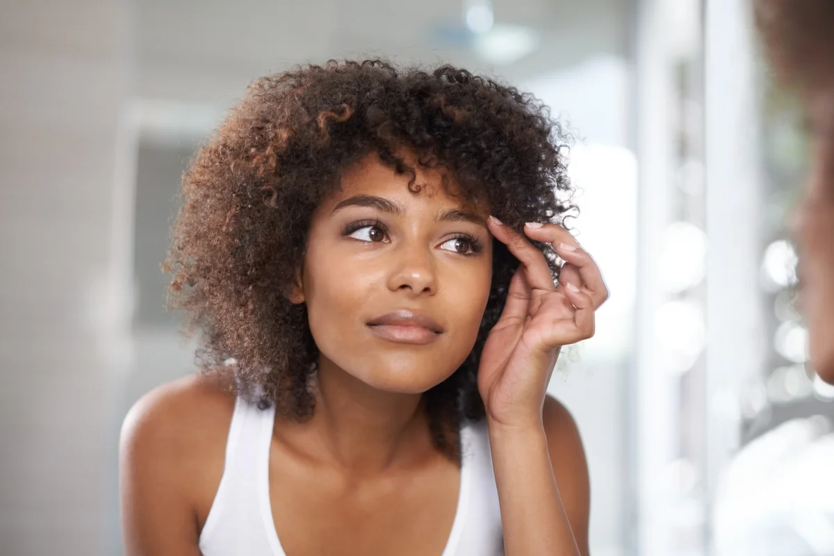 Mulher cuida das sobrancelhas diante do espelho