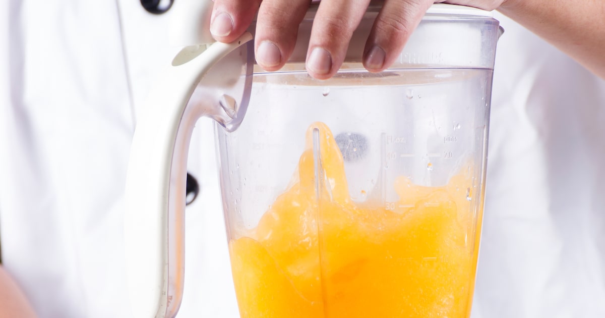 Liquidificador com suco de laranja e pedaços de laranja sobre a bancada