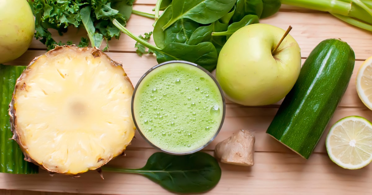 Suco verde em copo de vidro com abacaxi, limão, pepino e maçã sobre mesa de madeira