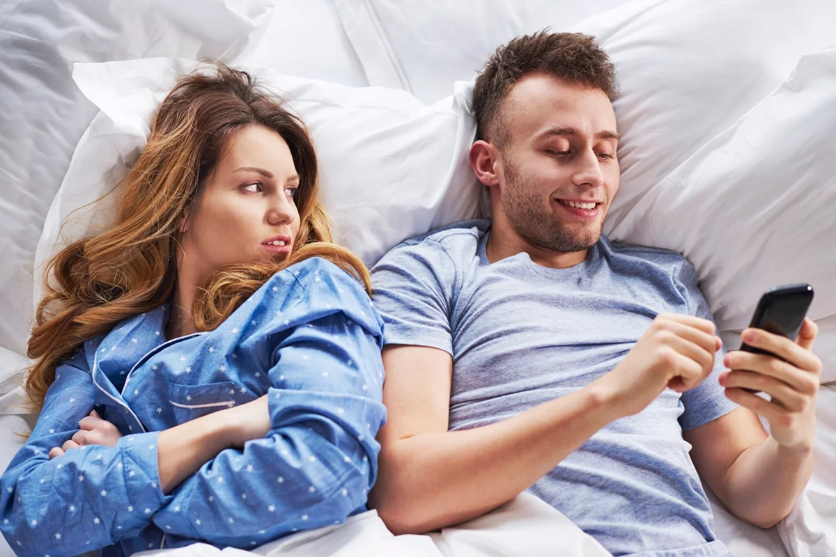 Casal sentado lado a lado enquanto uma pessoa usa o celular
