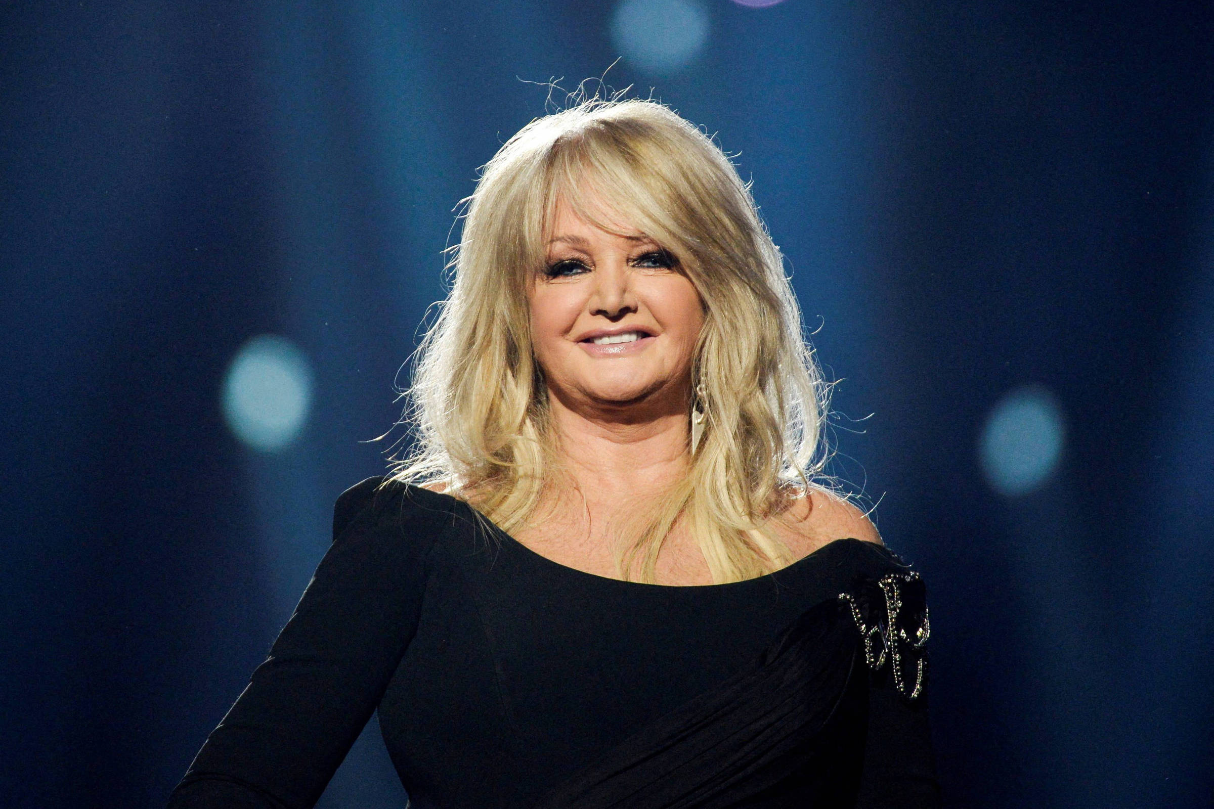 Bonnie Tyler sorrindo no palco com vestido preto
