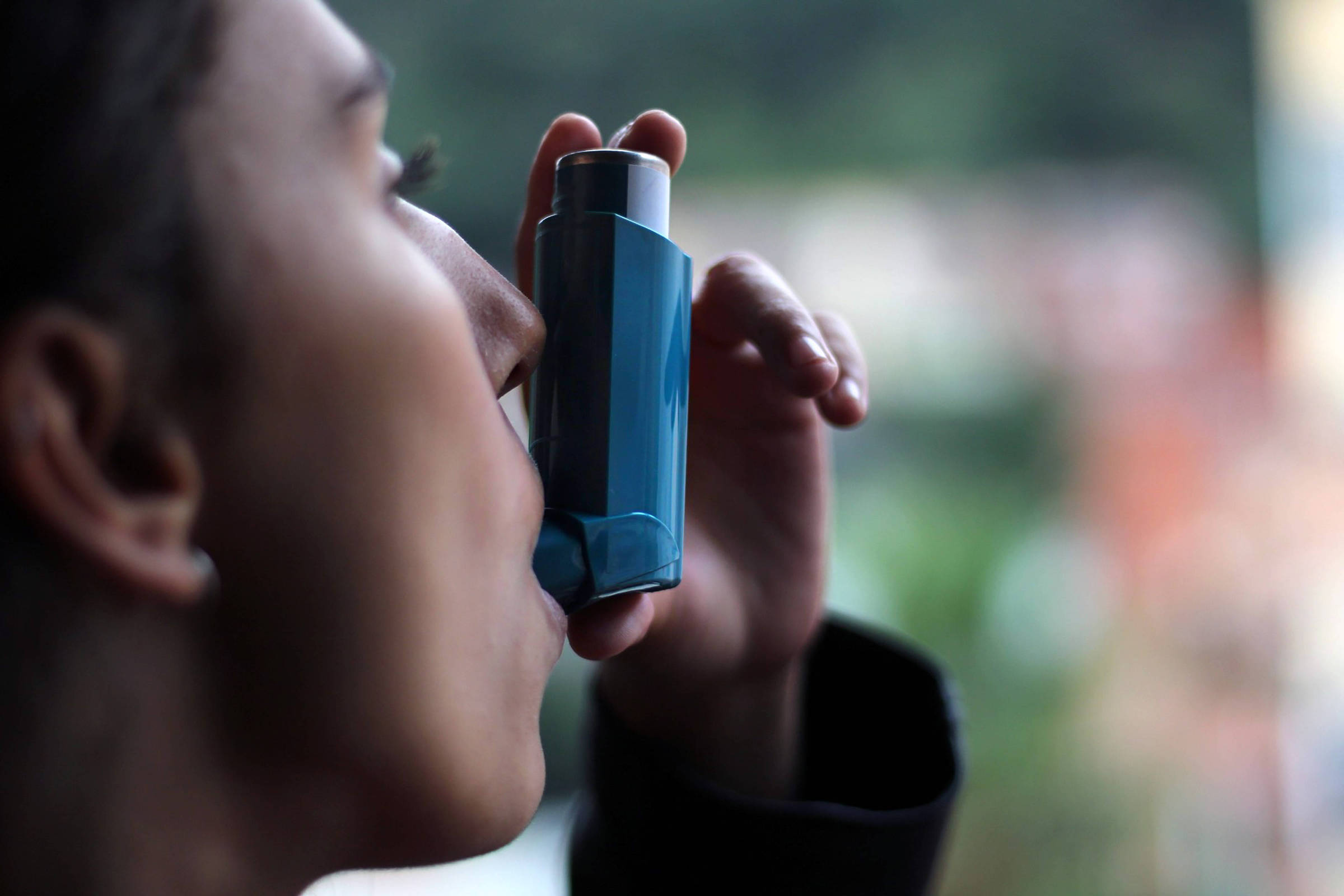 Jovem usa inalador azul para controlar sintomas de asma